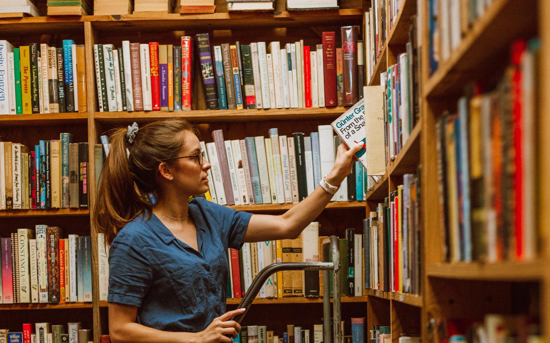 Junge Frau auf einer Leiter vor dem Bücherregal